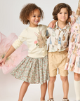 Three children wearing floral and patterned clothing with a soft, neutral background.