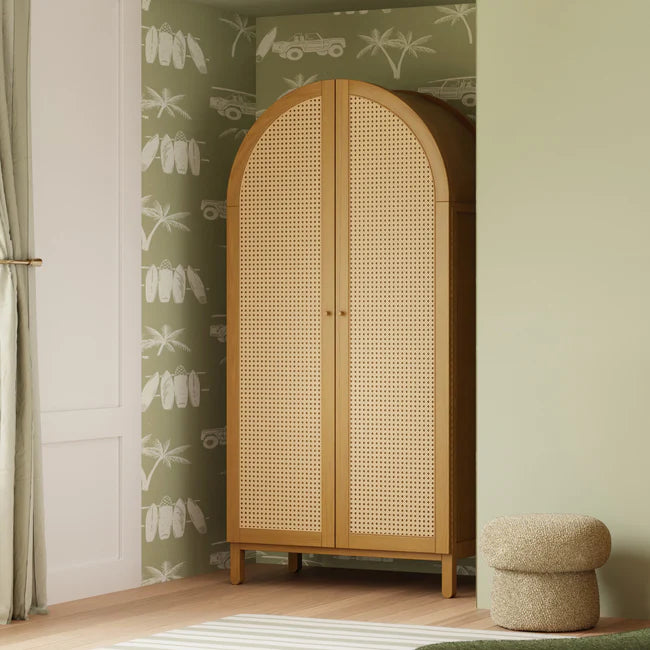 Wooden wardrobe with wicker doors in a room with patterned wallpaper and a small ottoman.