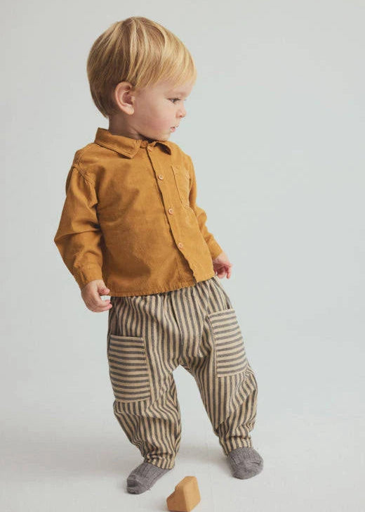 Child wearing a mustard yellow shirt and striped pants on a plain background