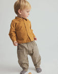 Child wearing a mustard yellow shirt and striped pants on a plain background