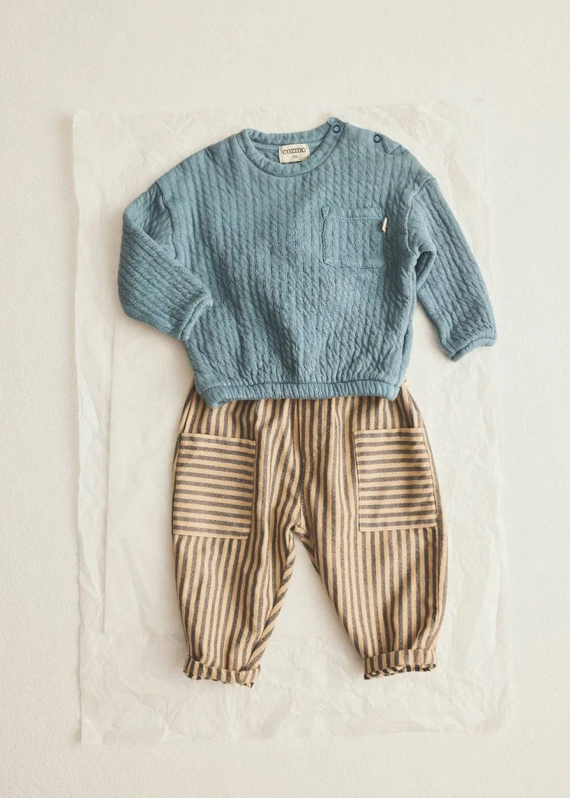 A baby outfit set consisting of a light blue cable-knit long-sleeve top and beige-and-brown vertically striped pants with patch pockets, laid flat on a white sheet of paper against a light beige background.