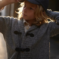 Child wearing a gray coat and blue cap with a blurred background