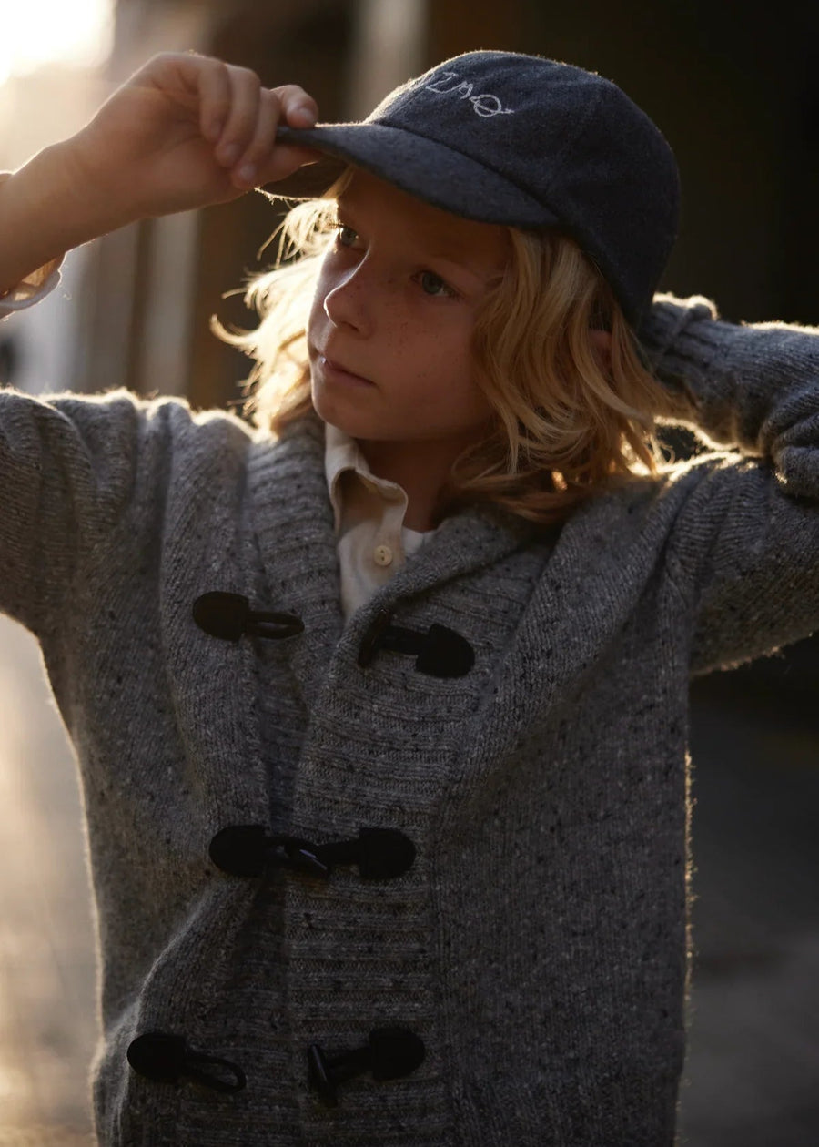 Child wearing a gray coat and blue cap with a blurred background