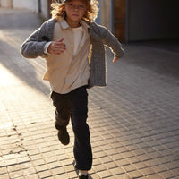 Child running on a brick sidewalk wearing a gray coat and cap.