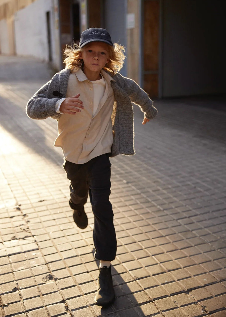 Child running on a brick sidewalk wearing a gray coat and cap.