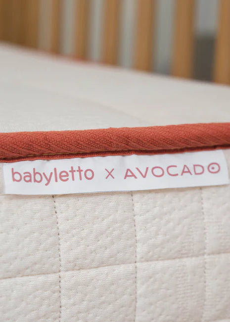 Close-up of a baby crib mattress with 'babyletto x AVOCADO' label.