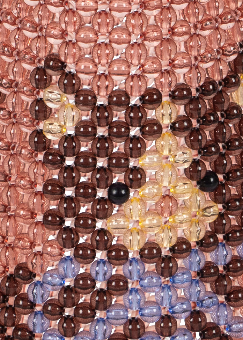 A close-up of a beaded textile or wall art piece featuring a stylized face made of translucent glass beads. The design includes a dusty rose background, dark brown and amber facial features, and light blue beads along the bottom edge.