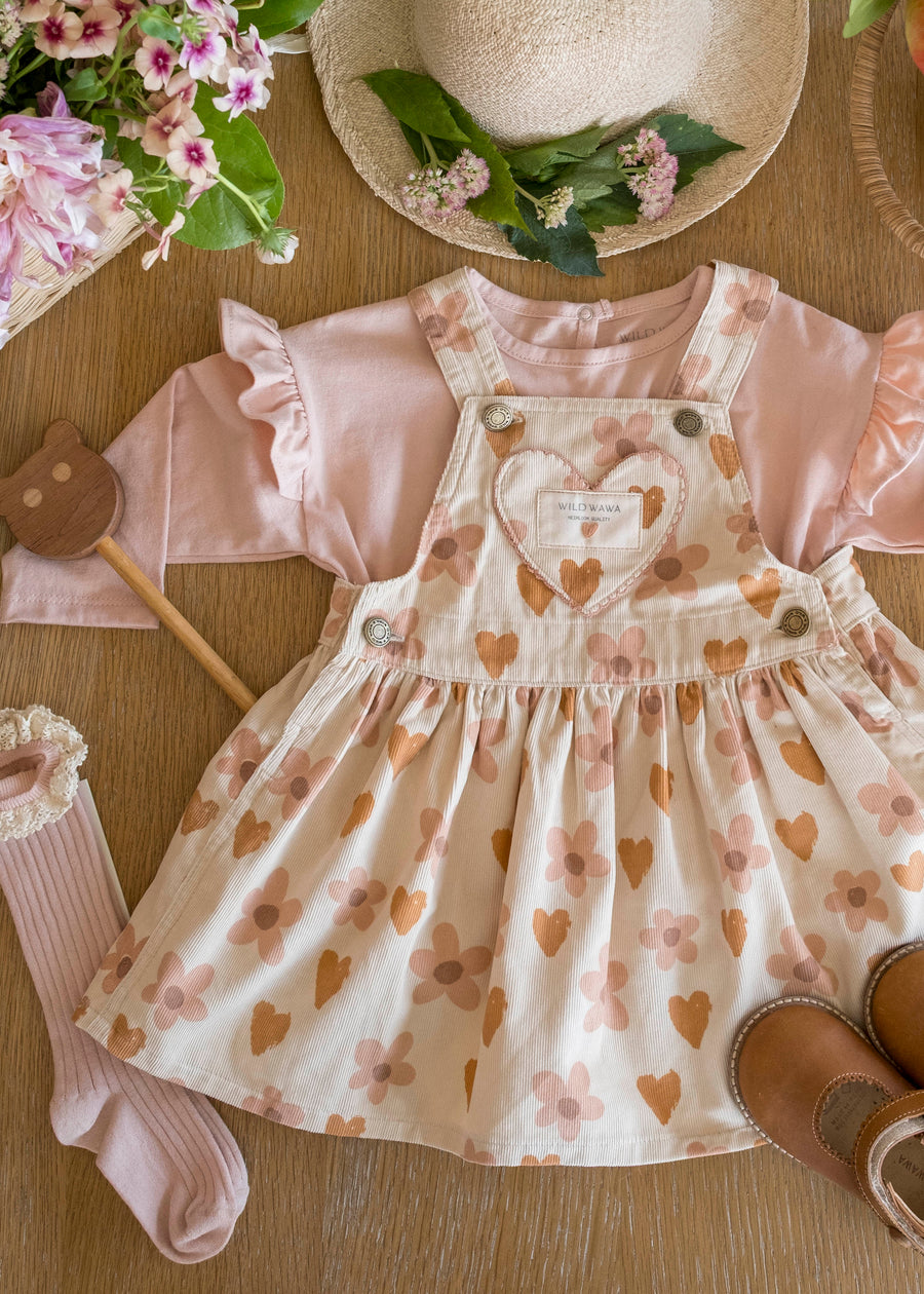 Children's dress with heart and flower pattern, surrounded by accessories on a wooden surface.