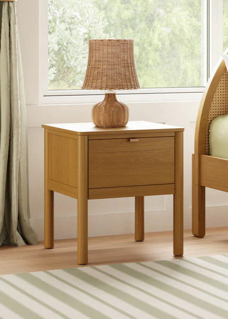 Wooden nightstand with a lamp next to a bed in a bedroom setting