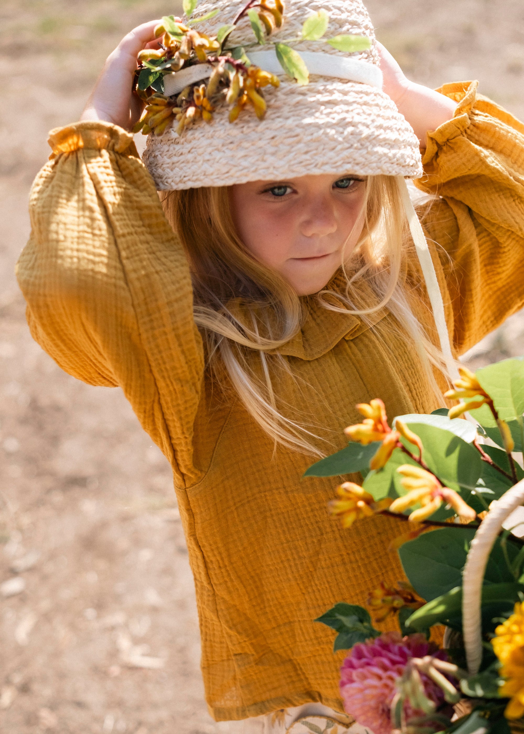 Child in a yellow outfit with a straw hat holding flowers outdoors