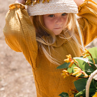 Child in a yellow outfit with a straw hat holding flowers outdoors