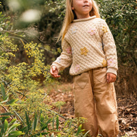 Young girl in a forest wearing a patterned sweater and beige pants.