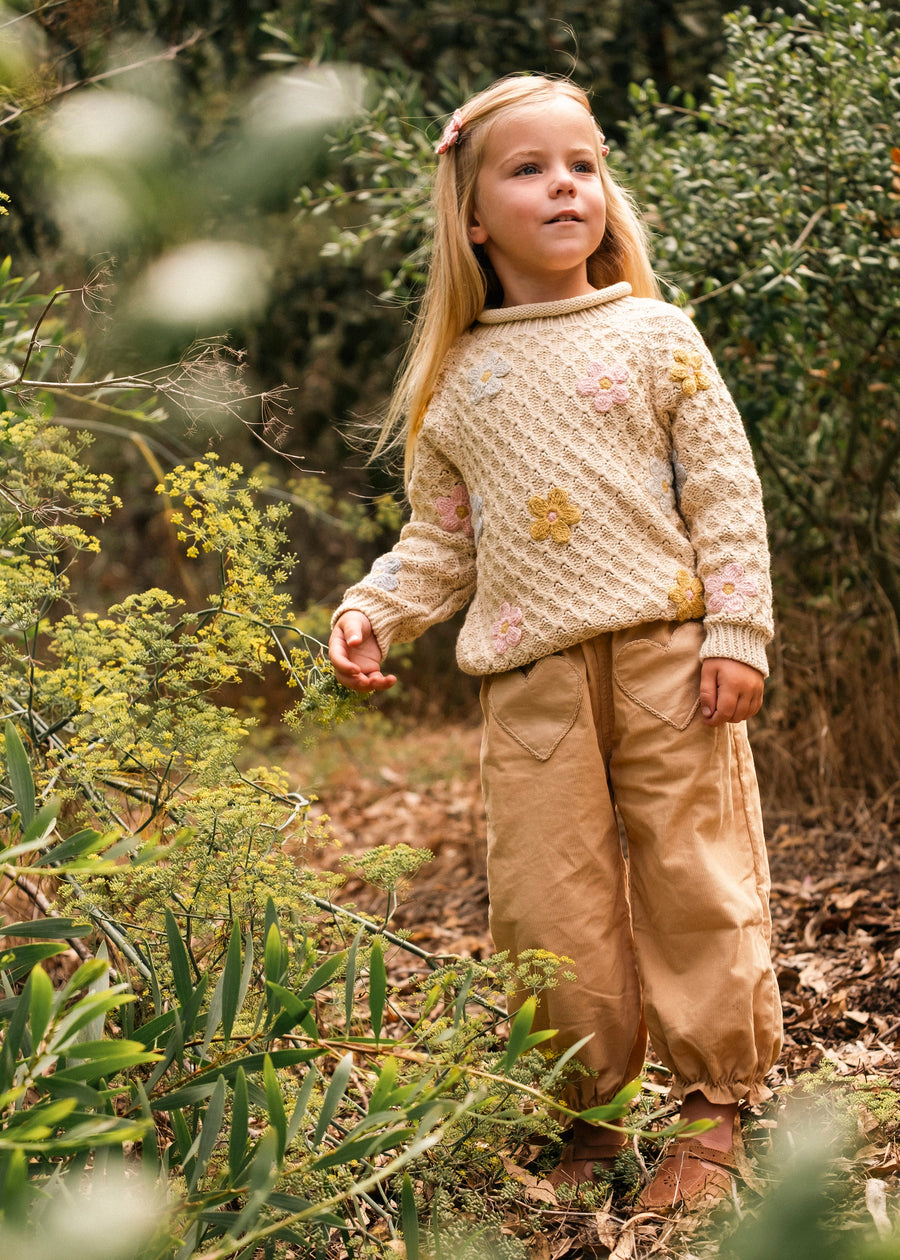 Young girl in a forest wearing a patterned sweater and beige pants.