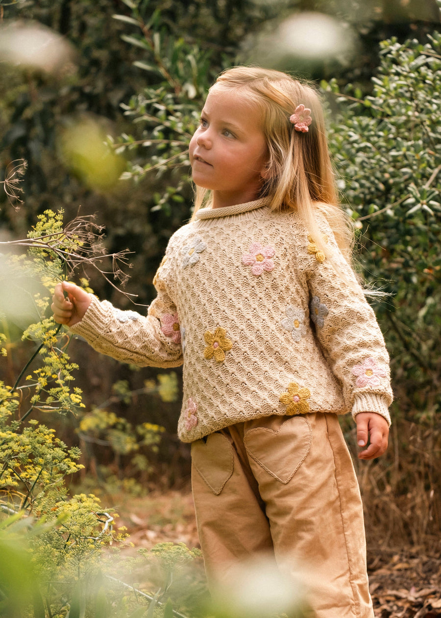 Young girl in a beige sweater and brown pants standing in a forest setting