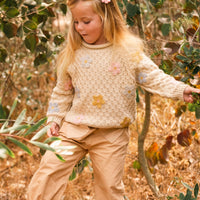 Young girl in a natural setting wearing a patterned sweater and beige pants.