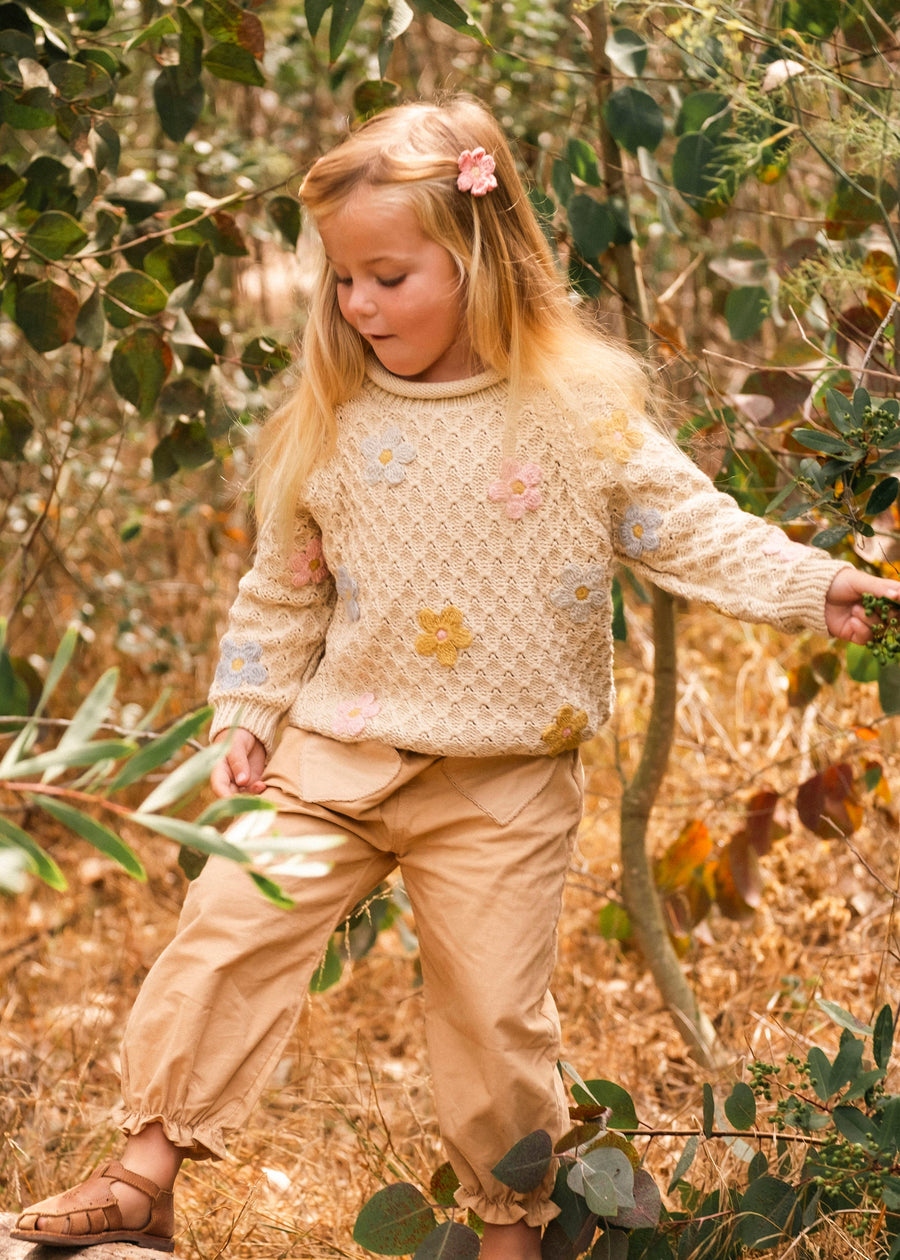 Young girl in a natural setting wearing a patterned sweater and beige pants.